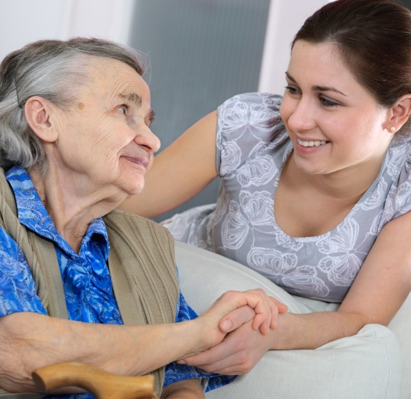 A female occupational therapist shares a smile with an elderly female woman while holding hands.