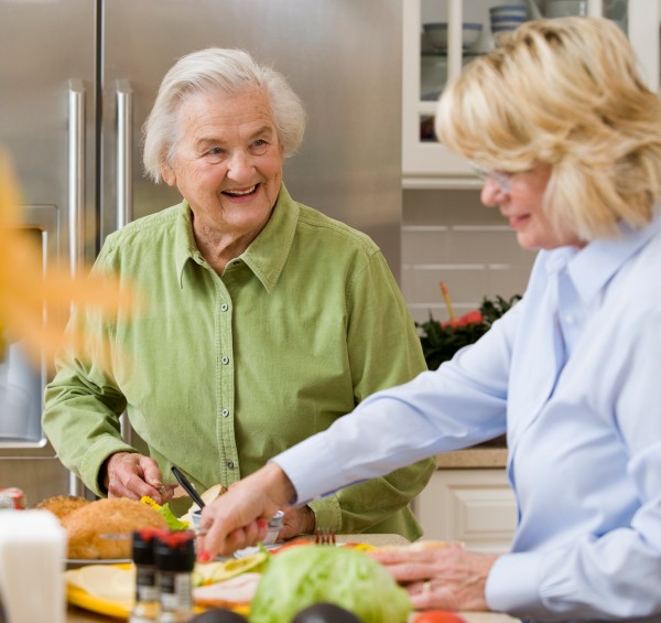 A senior woman smiles and talks with her OT while preparing some food in her home.